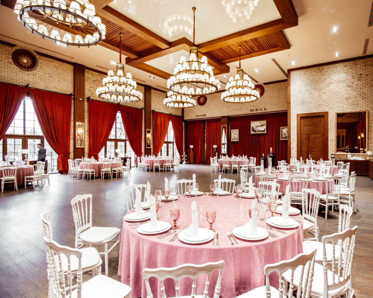 restaurant hall with round tables white napoleon chairs red curtains brick walls and chandeliers